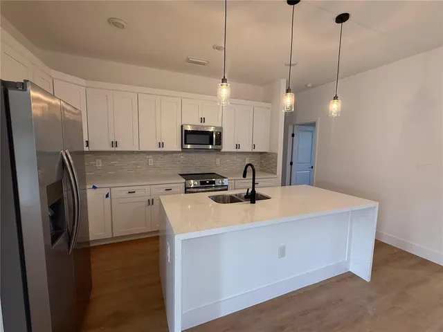 a kitchen with stainless steel appliances granite countertop a sink a stove a refrigerator a center island with cabinets and wooden floor