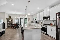 a kitchen with stainless steel appliances kitchen island granite countertop a stove top oven a sink a dining table and chairs with wooden floor