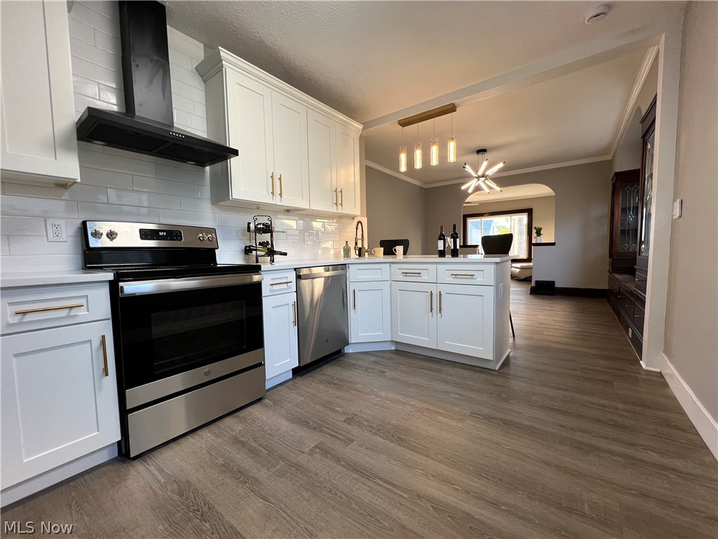 4523 Maplecrest Avenue Parma, OH 44134 - Photo 11 of 31 Kitchen with kitchen peninsula, crown molding, wall chimney exhaust hood, wood-type flooring, and appliances with stainless steel finishes