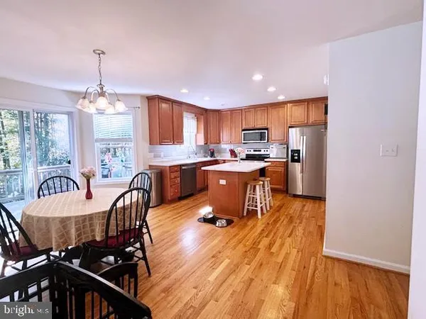 a kitchen with stainless steel appliances granite countertop a stove top oven a refrigerator a dining table and chairs with wooden floor