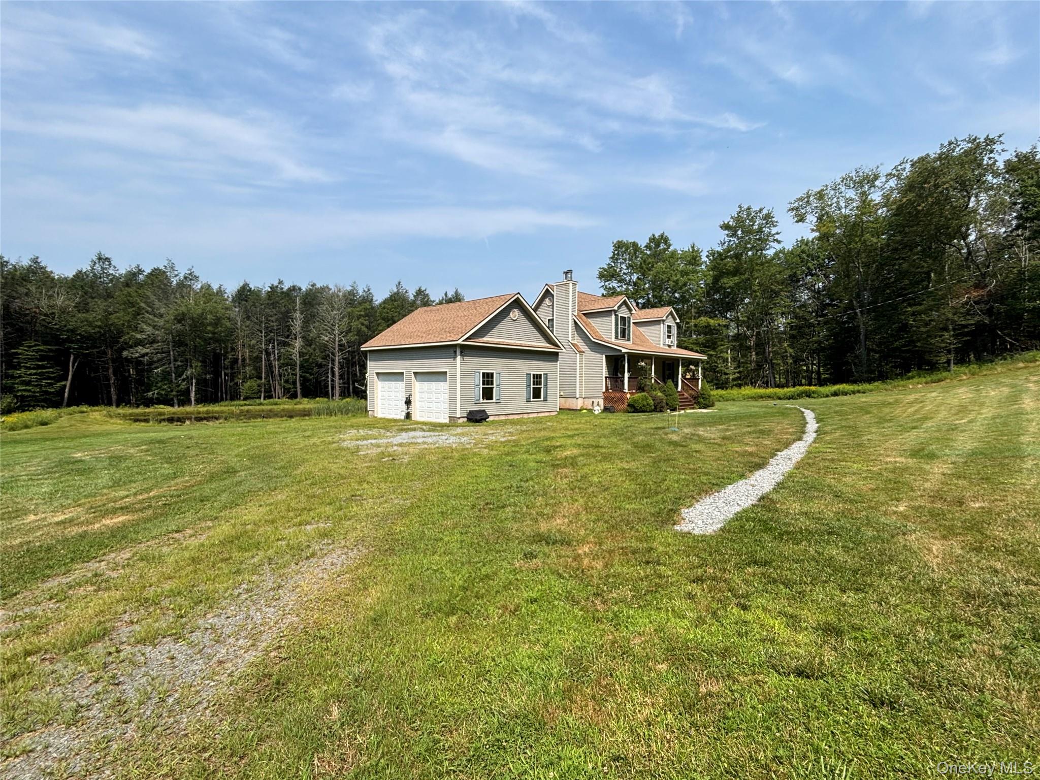 Rear view of property with driveway, a yard, a forest view, a chimney, and a garage