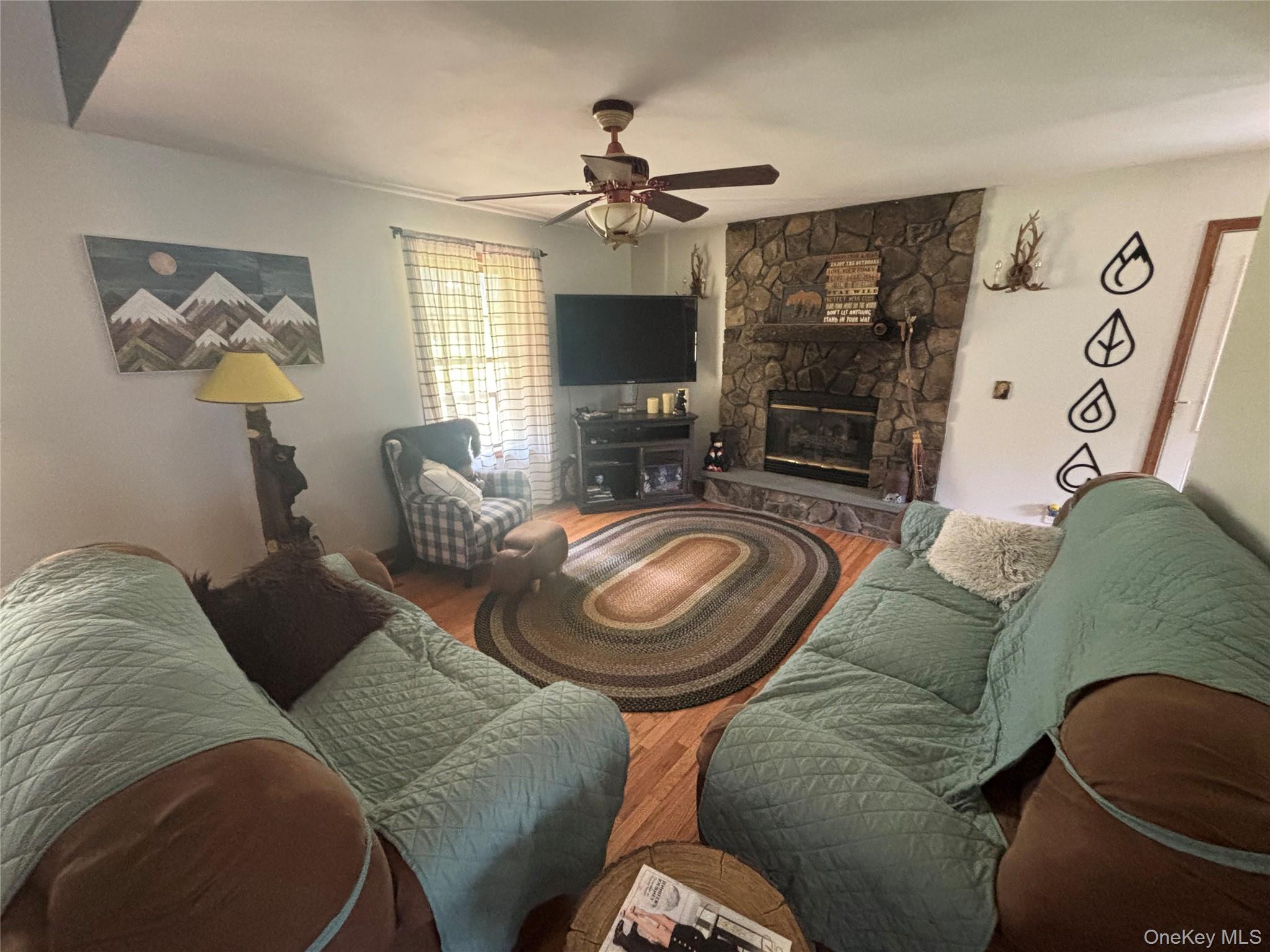595 Hurd And Parks Road Swan Lake, NY 12783 - Photo 13 of 43 Living room featuring a stone fireplace, wood finished floors, and ceiling fan