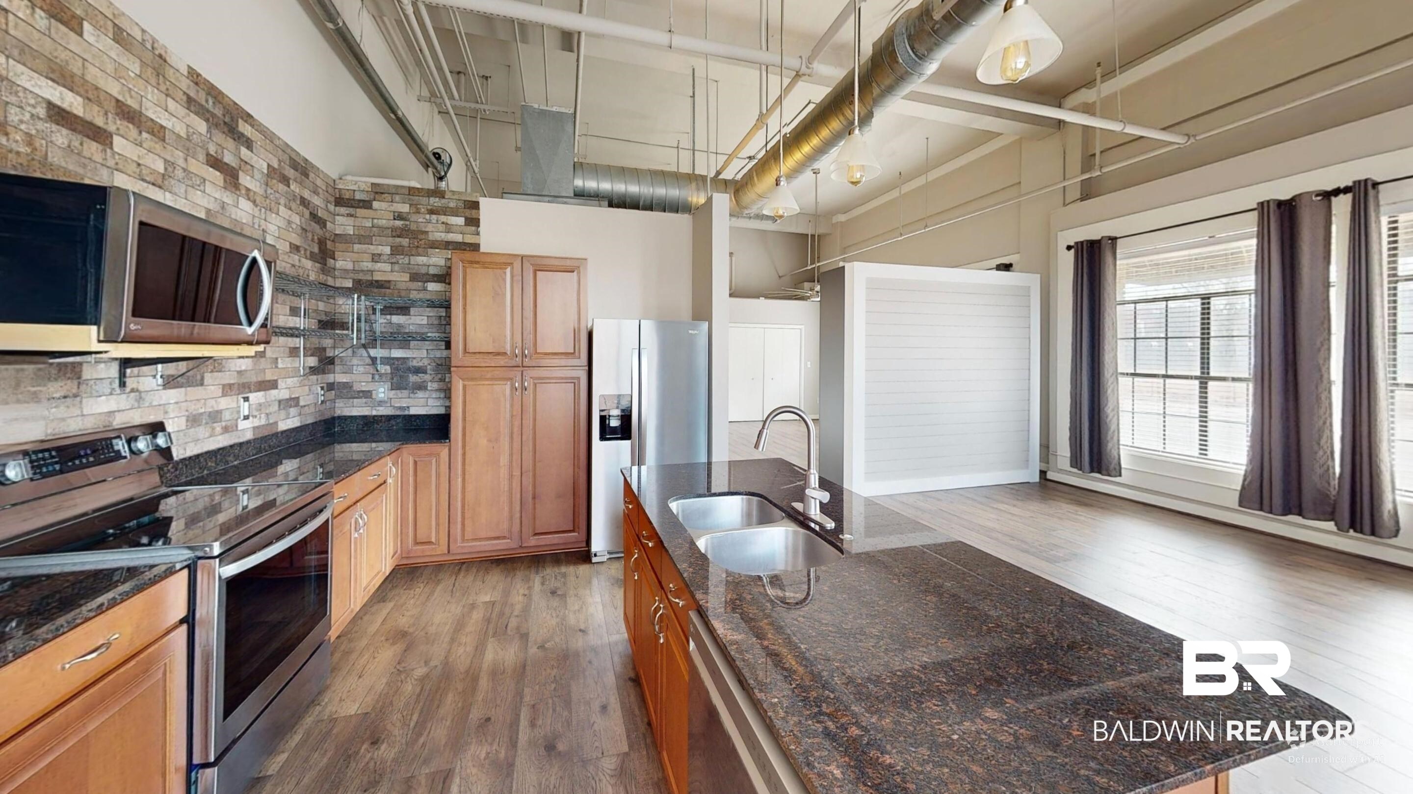 308 St Louis Street, Unit 101 Mobile, AL 36602 - Photo 28 of 30 Kitchen featuring stainless steel appliances, dark wood finished floors, a high ceiling, dark stone countertops, and brown cabinets
