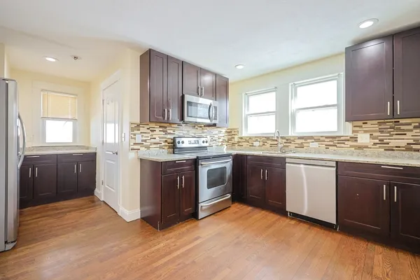 a kitchen with stainless steel appliances granite countertop a stove a sink dishwasher a refrigerator and white cabinets with wooden floor