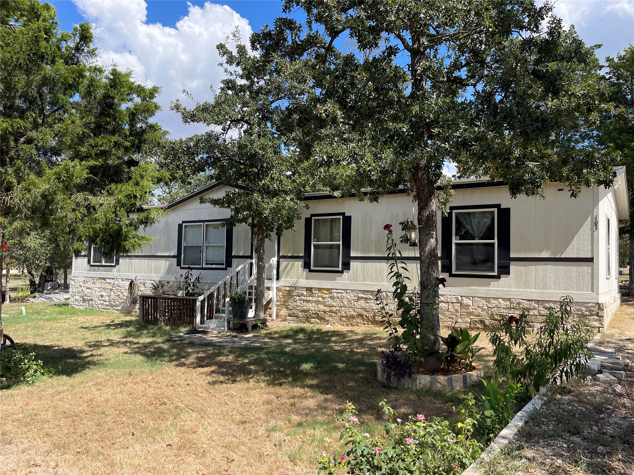 103 Azalea Avenue Elgin, TX 78621 - Photo 15 of 23 Mature trees frame this classic exterior featuring stone accents and decorative shutters.