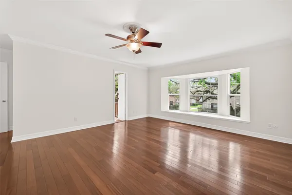 a view of an empty room with wooden floor and a ceiling fan