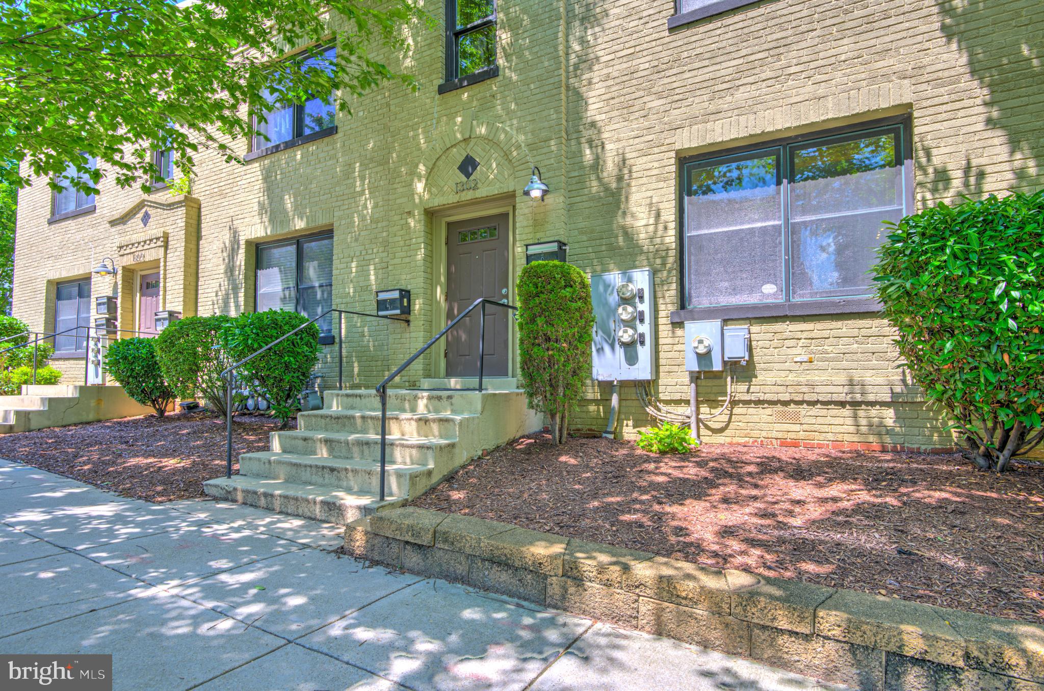 a view of a brick house with many windows plants and large tree