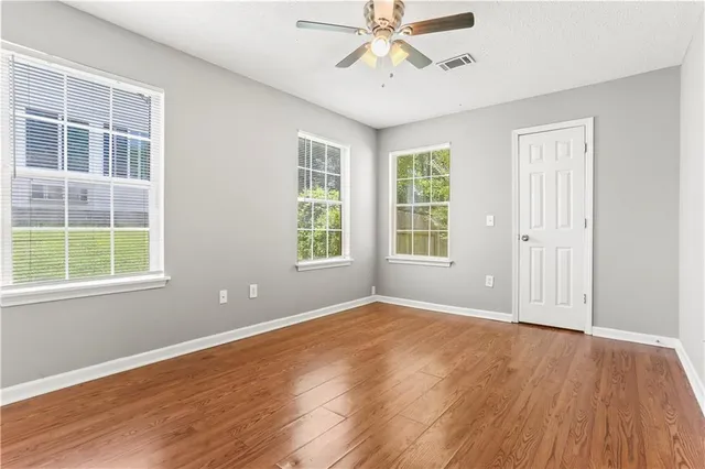 an empty room with wooden floor chandelier fan and windows