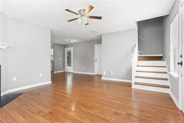 a view of an empty room with wooden floor and a ceiling fan