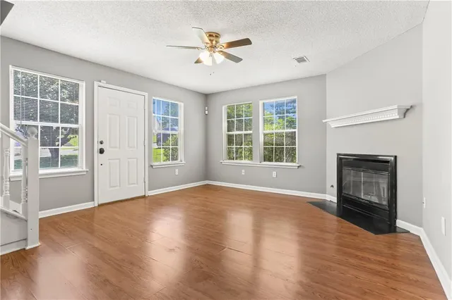 an empty room with wooden floor a ceiling fan and windows