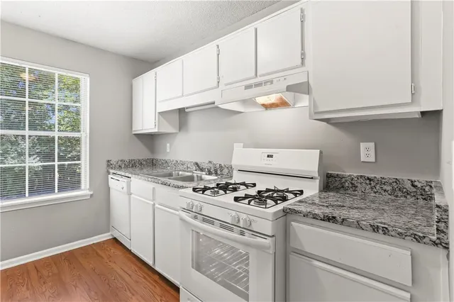a kitchen with granite countertop white cabinets and a stove with wooden floor