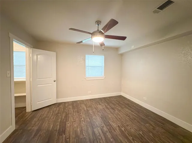an empty room with wooden floor chandelier fan and windows