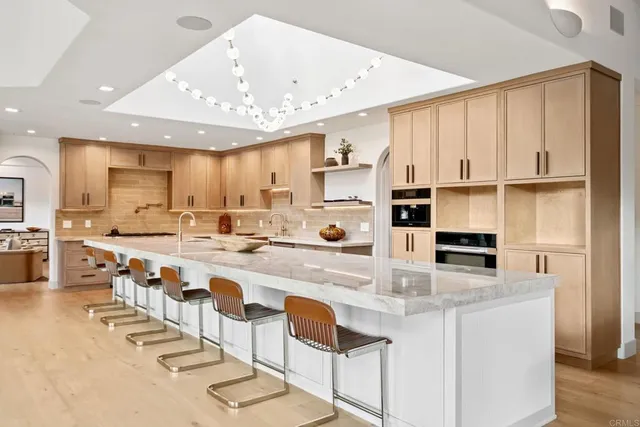 a kitchen with stainless steel appliances granite countertop a stove top oven a sink a refrigerator white cabinets and chairs with wooden floor