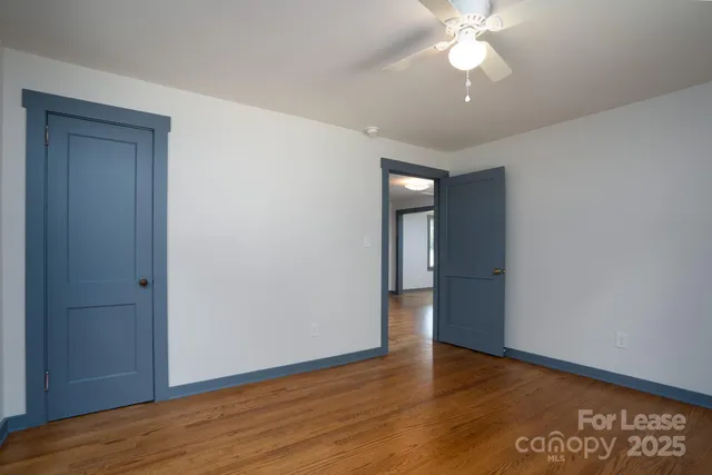 a view of an empty room with wooden floor and a chandelier fan