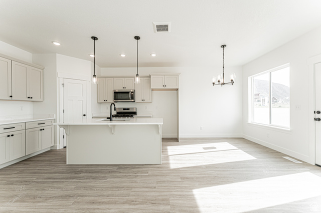 4774 Alder Drive Mapleton, UT 84664 - Photo 6 of 27 Kitchen with hanging lights, light wood-type flooring, a kitchen breakfast bar, stainless steel appliances, and light stone counters
