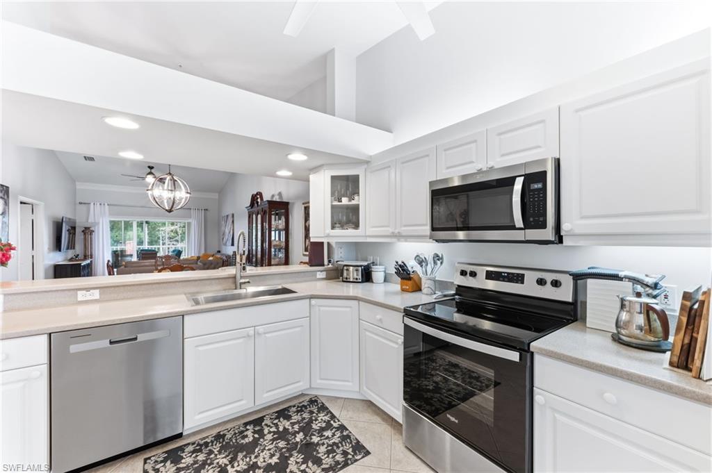 6840 Beach Resort Drive, Unit 16 Naples, FL 34114 - Photo 16 of 49 Kitchen with stainless steel appliances, white cabinets, vaulted ceiling, hanging lights, and glass fronted cabinets