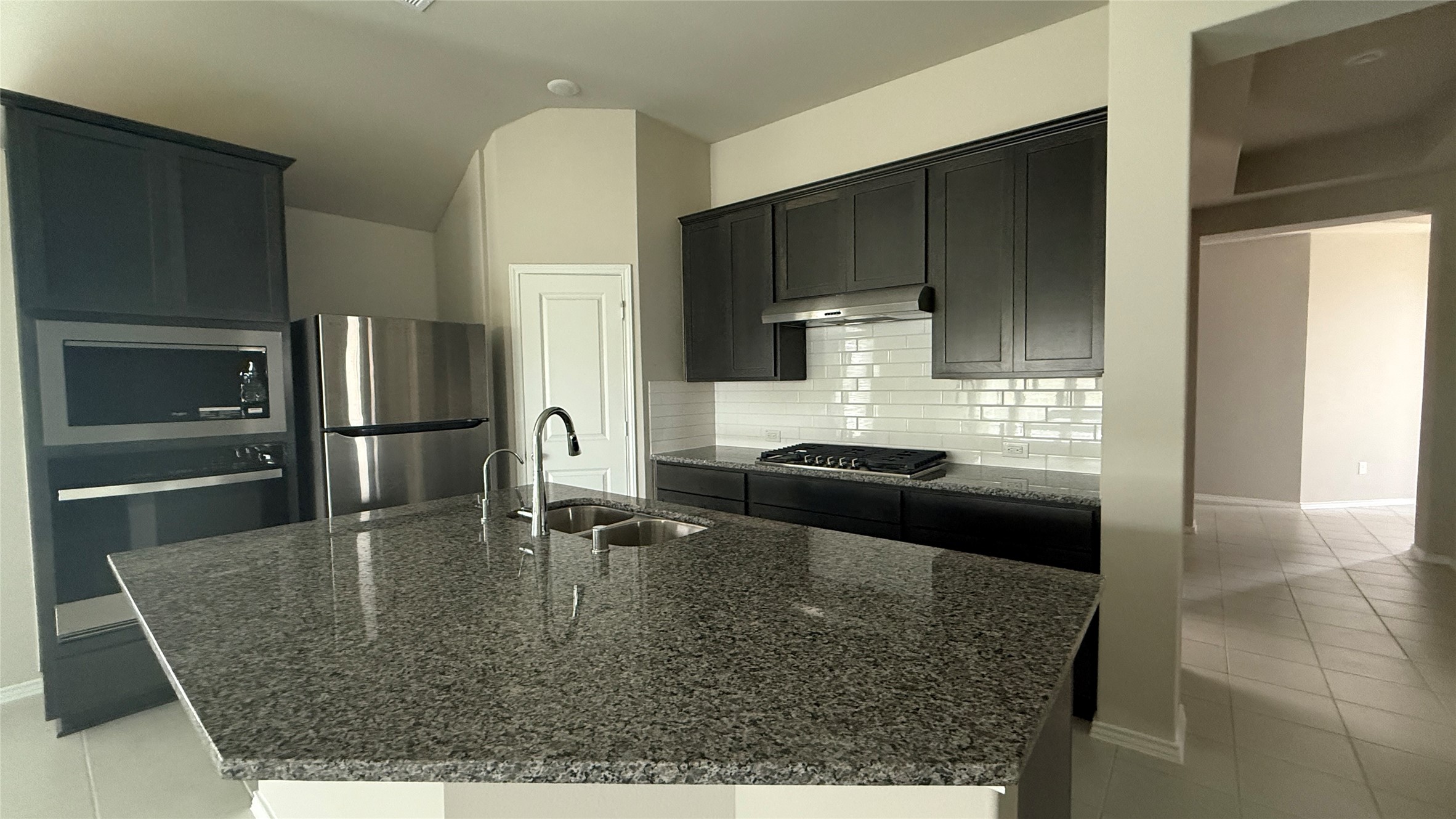 31961 Retama Rnch Drive Spring, TX 77386 - Photo 10 of 25 This modern kitchen features sleek dark cabinetry, a large granite island with a sink, stainless steel appliances, and a stylish subway tile backsplash. Ideal for cooking and entertaining.