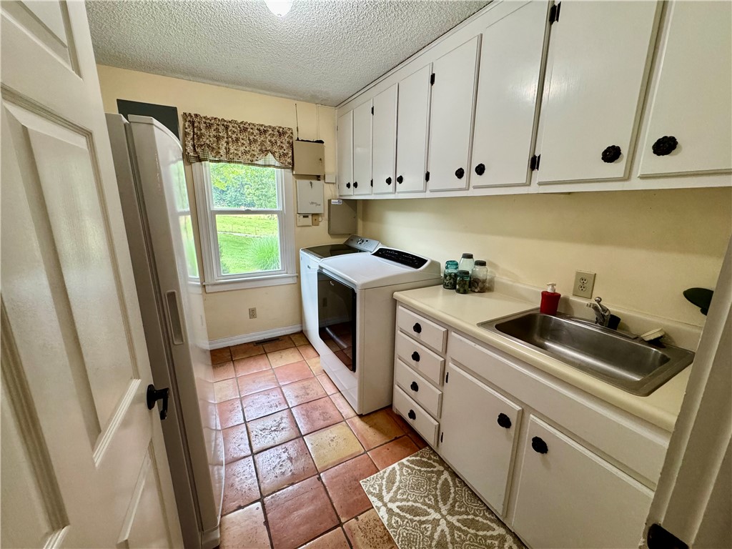 15196 Cincinnati Creek Road Summers, AR 72769 - Photo 23 of 42 Utility room featuring terra cotta style tile flooring, white cabinetry with black hardware, a stainless steel sink, and a double-hung window