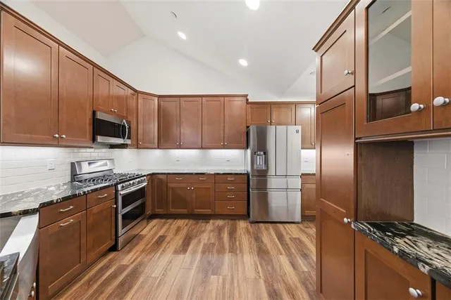 a large kitchen with a stove a sink dishwasher a refrigerator and wooden cabinets with wooden floor