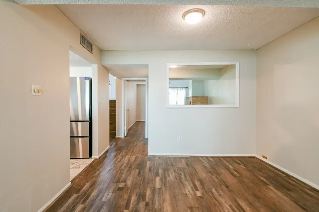 an empty room with wooden floor and a kitchen