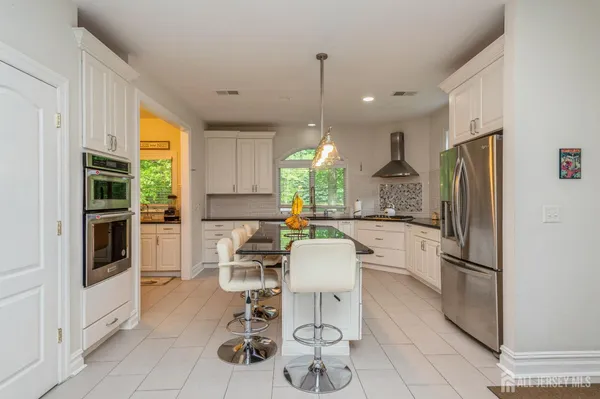 a kitchen with stainless steel appliances kitchen island granite countertop a refrigerator a stove a dining table and chairs with wooden floor