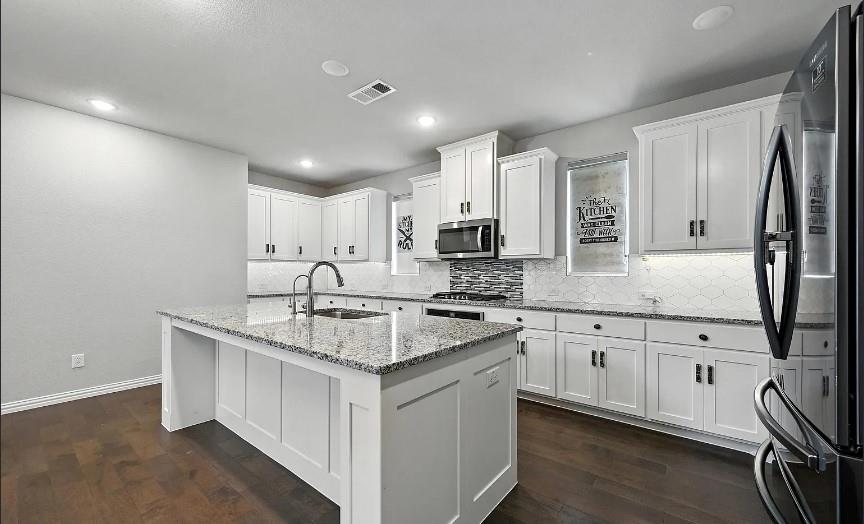 12559 Ravine Creek Road Frisco, TX 75035 - Photo 7 of 33 Kitchen featuring freestanding refrigerator, white cabinetry, light stone countertops, an island with sink, and dark wood-style flooring