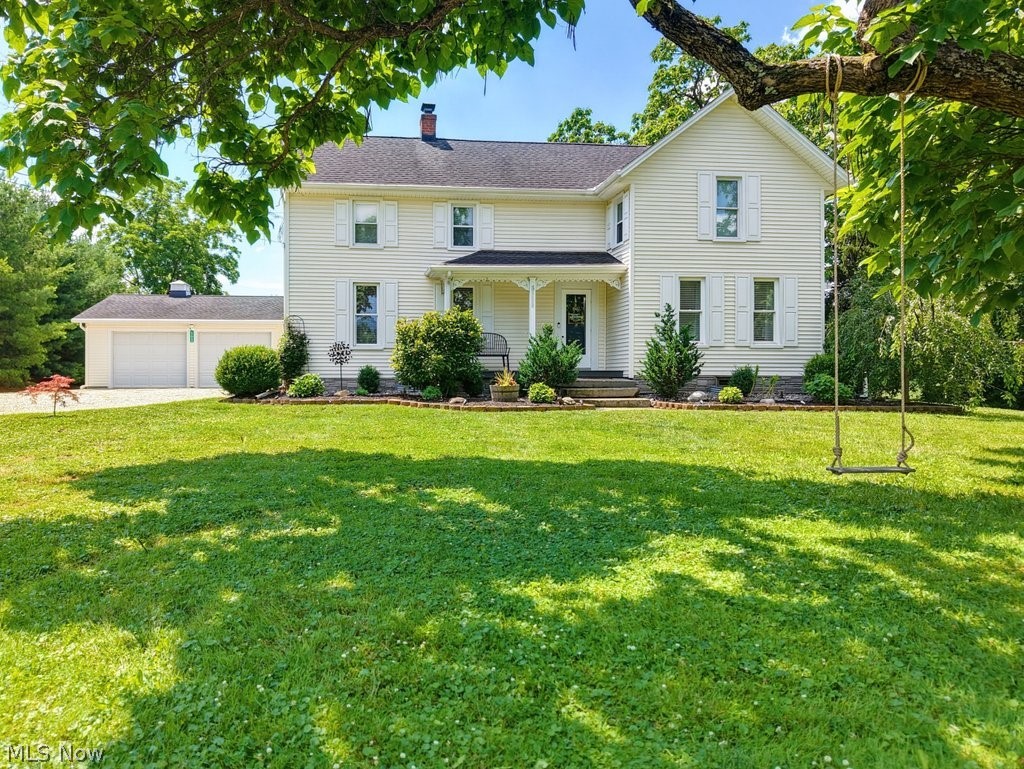 23055 Snell Road Columbia Station, OH 44028 - Photo 2 of 50 Classic cream-colored home with white louvered shutters, a covered front porch, a two-car garage, and a spacious front lawn with mature trees and established landscaping