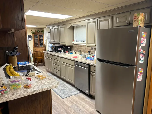 a kitchen with stainless steel appliances granite countertop a refrigerator a stove a sink dishwasher and white cabinets with wooden floor