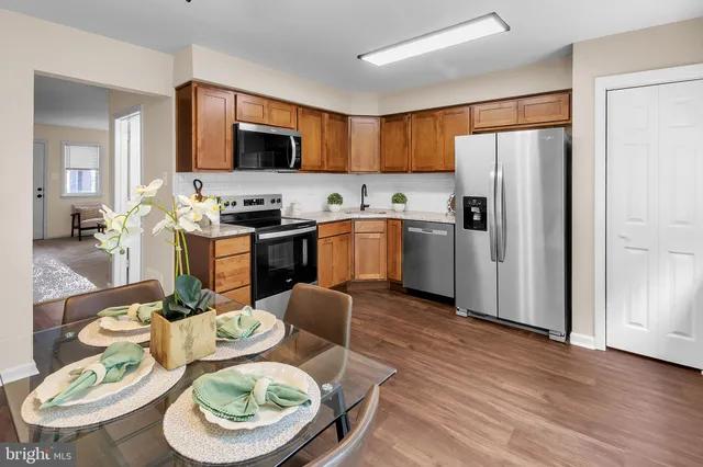 a kitchen with stainless steel appliances granite countertop a refrigerator a stove top oven a dining table and chairs with wooden floor