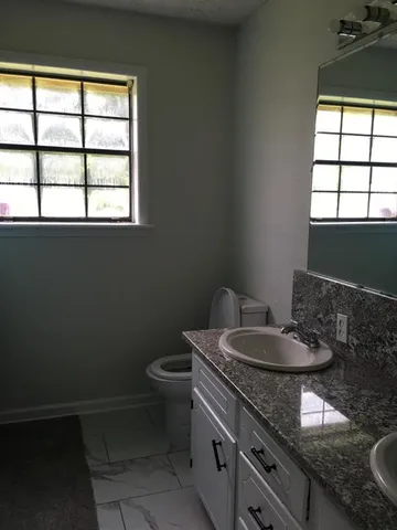 a bathroom with a granite countertop sink a toilet and a window