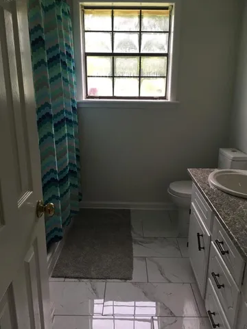a bathroom with a granite countertop sink a toilet a window and shower