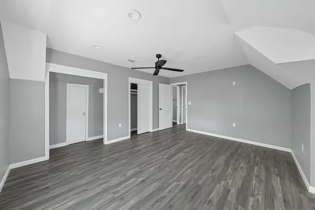 a view of an empty room with wooden floor and a ceiling fan