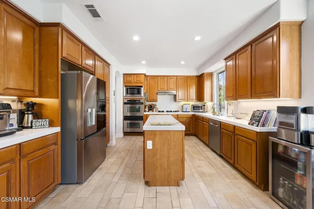a kitchen with stainless steel appliances granite countertop a refrigerator a sink dishwasher a stove top oven and a dining table with wooden floor