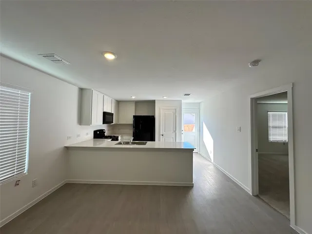 a living room with stainless steel appliances a kitchen island hardwood floor and a sink