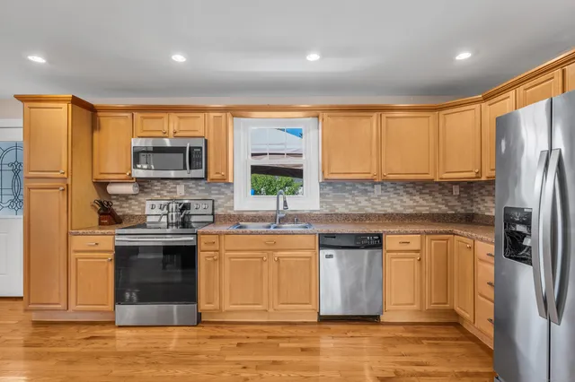 a kitchen with stainless steel appliances granite countertop a refrigerator a stove a sink and a microwave with wooden floor