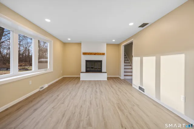 an empty room with wooden floor fireplace and windows
