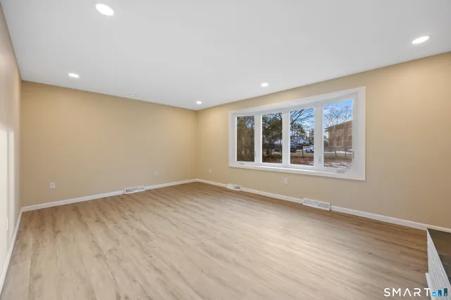 a view of an empty room with wooden floor and a window