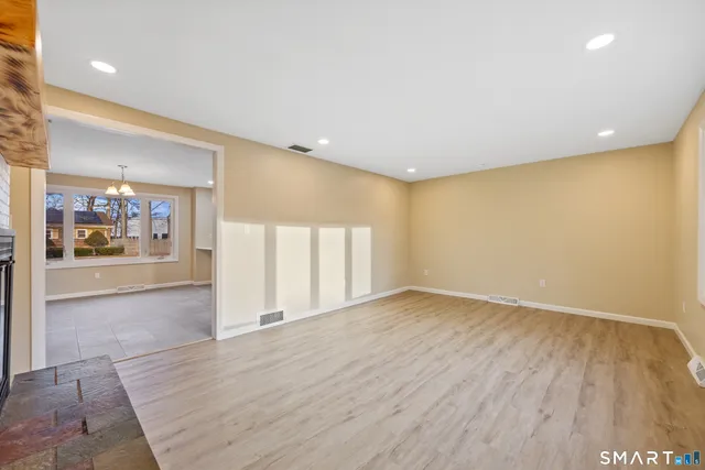 an empty room with wooden floor and way to kitchen