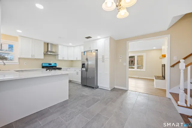 a kitchen with stainless steel appliances granite countertop a refrigerator a sink dishwasher a stove and white cabinets with wooden floor