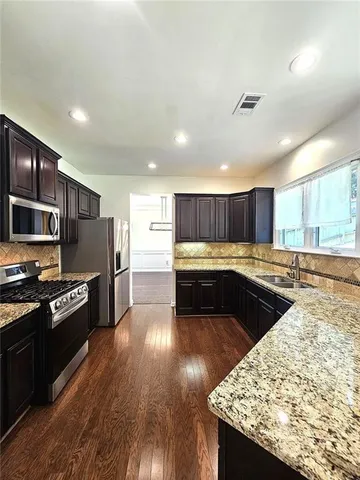 a kitchen with stainless steel appliances granite countertop a refrigerator a sink dishwasher a stove and white countertops with wooden floor