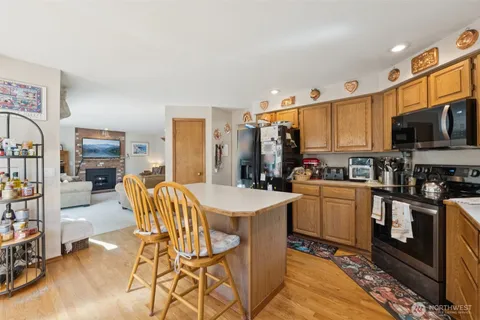 a kitchen with stainless steel appliances kitchen island granite countertop a refrigerator a stove a sink dishwasher and white cabinets with wooden floor