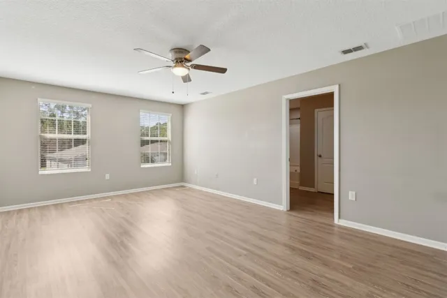 a view of an empty room with wooden floor and a ceiling fan