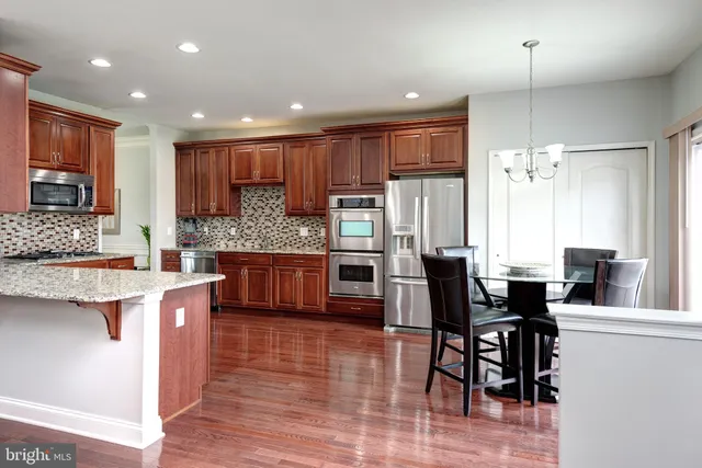 a kitchen with stainless steel appliances kitchen island granite countertop a stove a refrigerator a sink a dining table and chairs