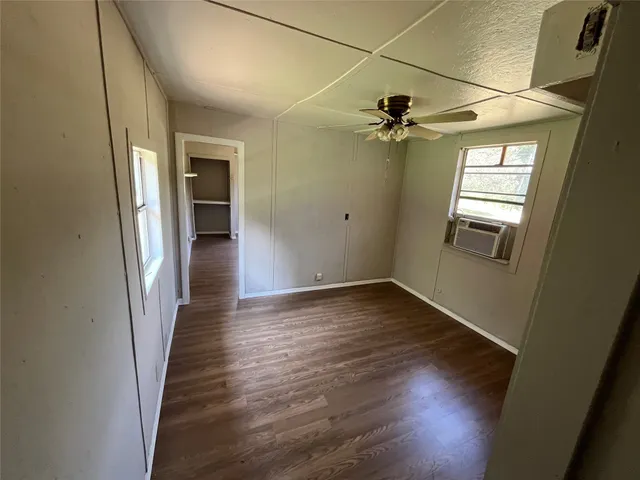 an empty room with wooden floor ceiling fan and windows