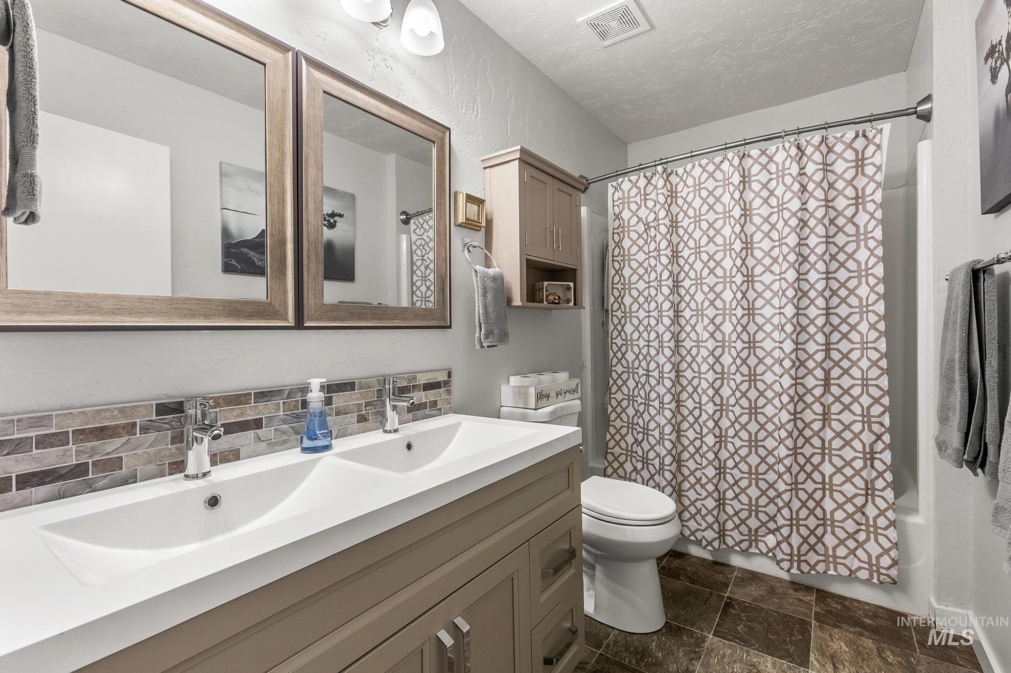 2208 Keithley Creek Road Midvale, ID 83645 - Photo 26 of 45 Bathroom featuring double vanity, tasteful backsplash, shower / bath combination with curtain, a textured ceiling, and stone finish floors