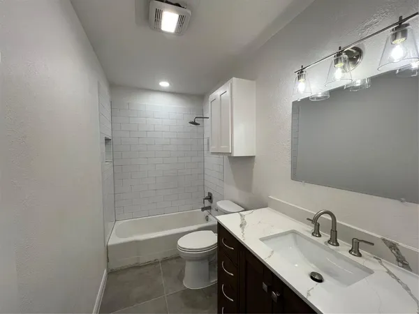 a bathroom with a bathtub shower sink vanity mirror and toilet