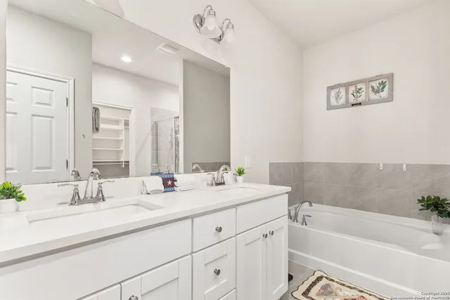 a bathroom with a double vanity sink a mirror a bathtub and next