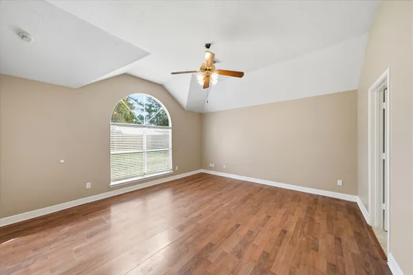 an empty room with wooden floor chandelier fan and windows