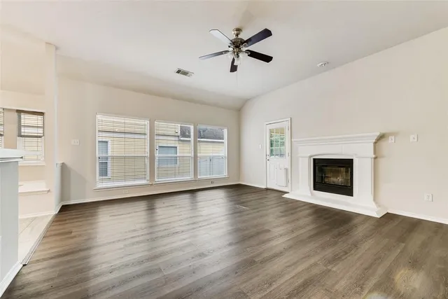 an empty room with wooden floor a ceiling fan and windows