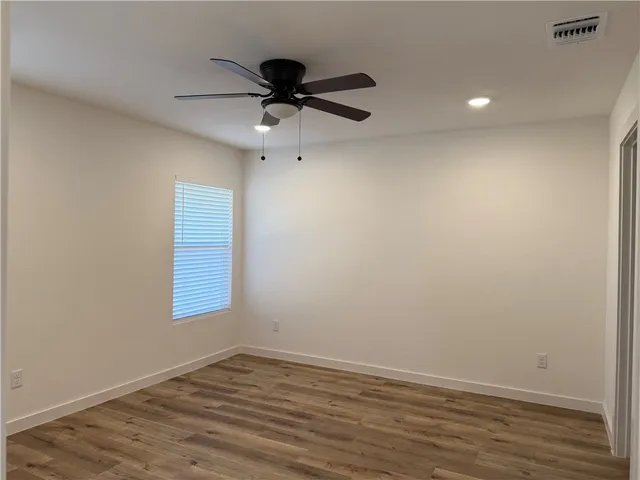 an empty room with wooden floor fan and windows